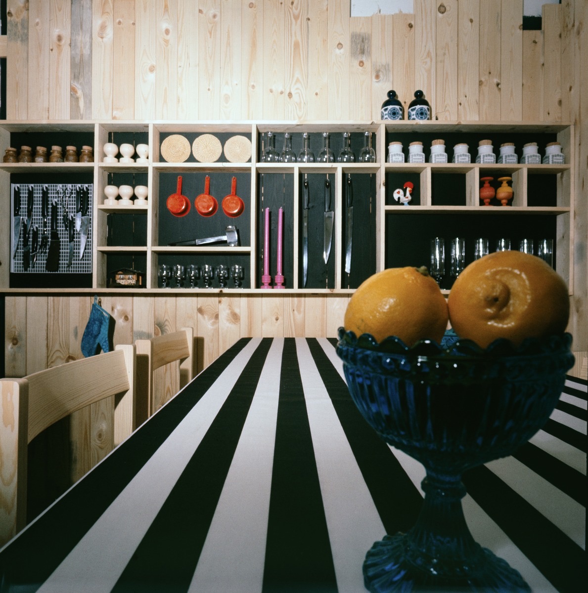 A navy blue Mariskooli bowl filled with lemons on a black-and-white striped table runner, in a 1966 Finnish kitchen