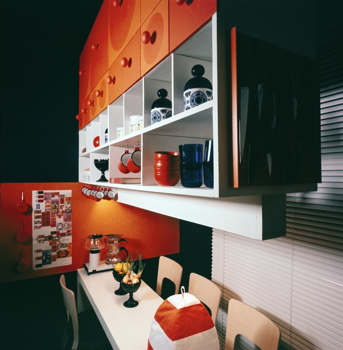 A black Mariskooli bowl on a table in a bold orange 1966 Finnish kitchen with built-in shelving